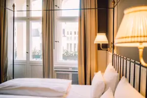 Gezellige hotelkamer bij HENRI Berlijn met hoge plafonds, lichte ramen en elegante bedlampjes in Wilhelminiaanse stijl.