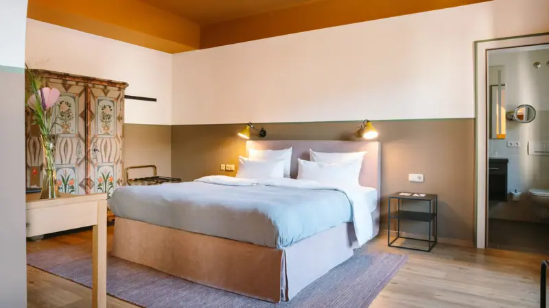 Een hotelkamer in het HENRI Garmisch-Partenkirchen met een groot knus bed, een oude kledingkast en een deur naar de aangrenzende badkamer.