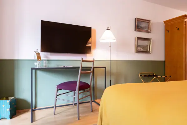Een hotelkamer in het HENRI Hotel in Garmisch-Partenkirchen met een bureau en een televisie aan de muur.