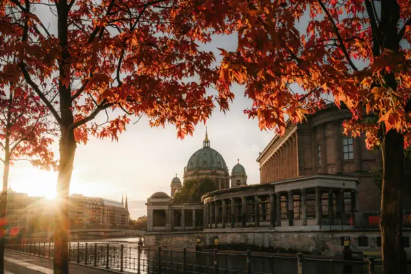 Een gebouw naast een rivier en een boom met rode bladeren in de herfst.