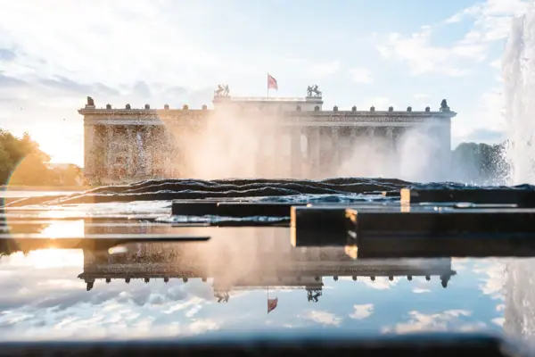 Het Altes Museum in Berlijn bij zonsondergang, gezien door de fonteinen van een fontein met een weerspiegeling op de voorgrond.
