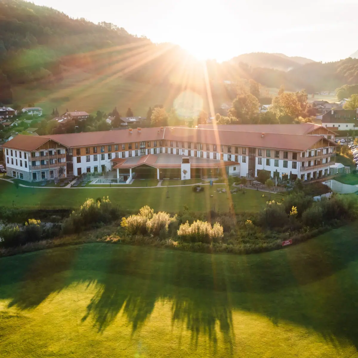 aja Hotel in Ruhpolding Luchtfoto van een groot hotel met een ruime tuin in het Alpenlandschap, zonnestralen schijnen over de heuvels en de ochtendhemel