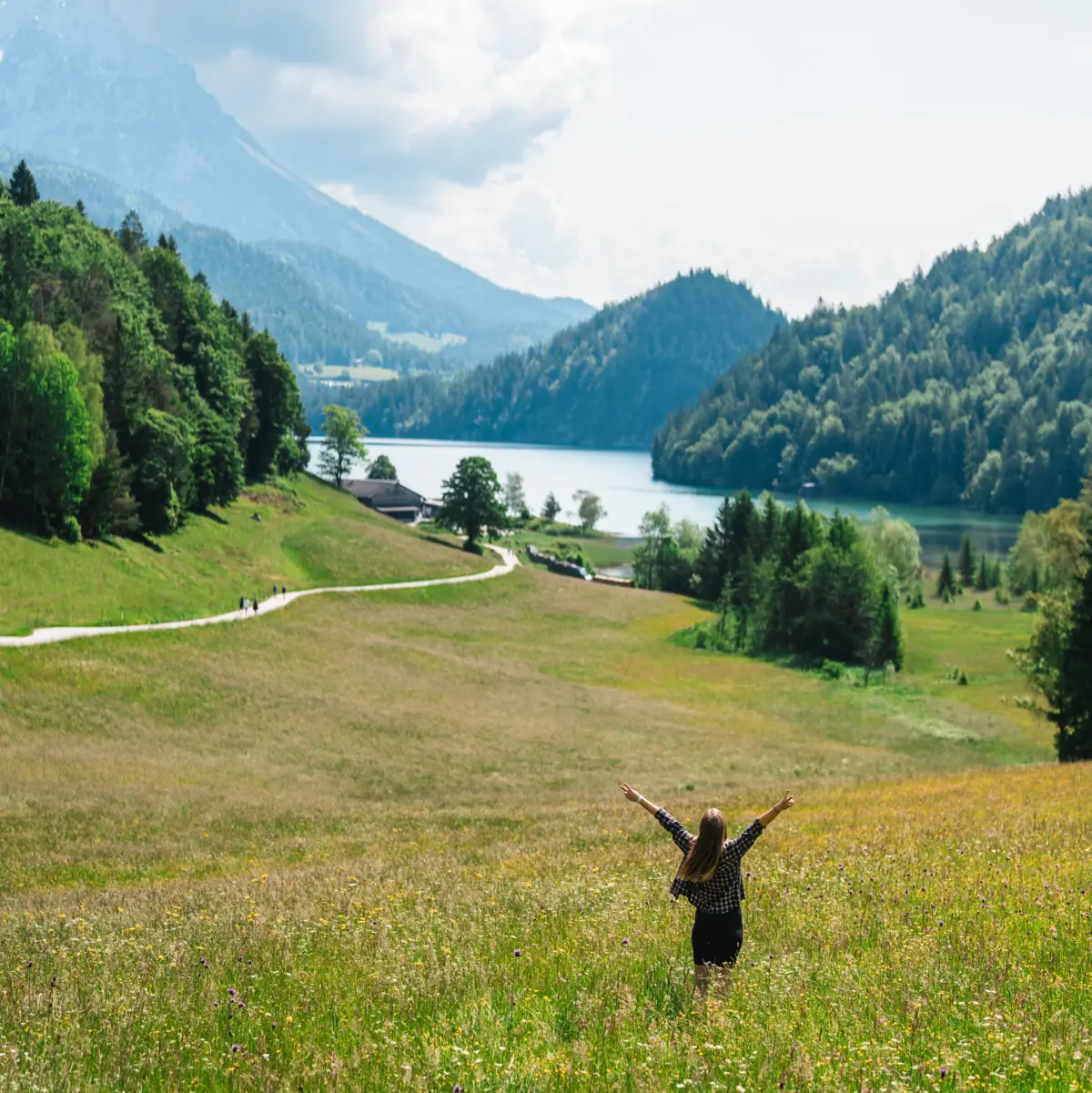 Vrouw staat op de alpenweiden en kijkt uit over het meer en de bergen.
