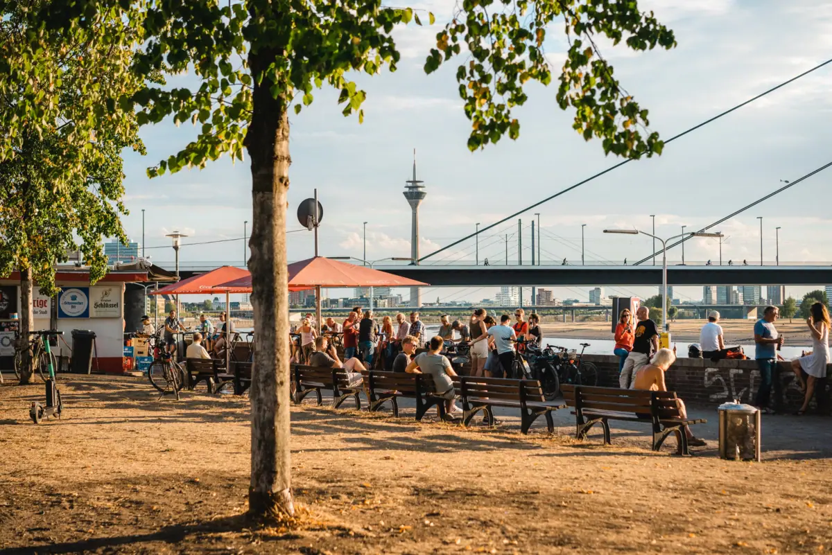 HENRI Düsseldorf Promenade Een groep mensen zit op bankjes in een park.