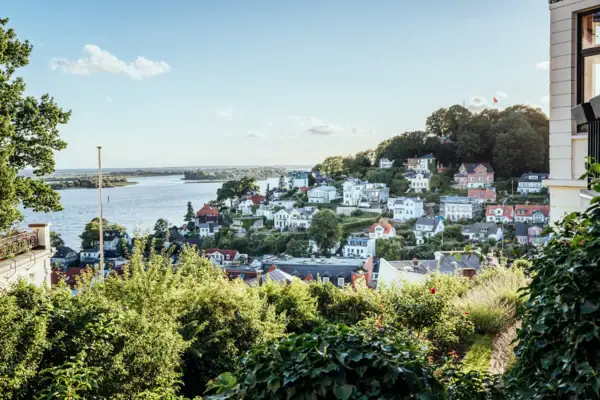 Stadsgezicht met water op de voorgrond, omringd door gebouwen en bomen onder een bewolkte hemel.