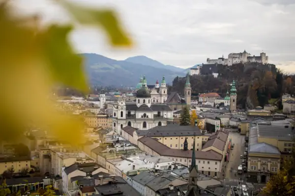 Een stad met veel gebouwen en een heuvel met bomen en bergen op de achtergrond.