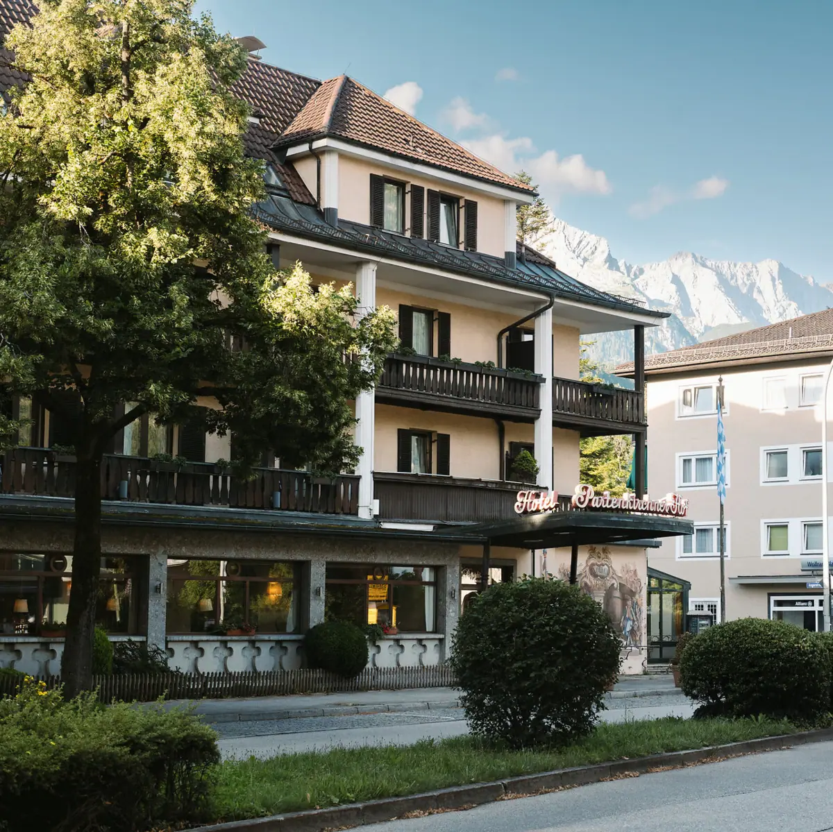 Het HENRI Hotel in Garmisch-Partenlkirchen met bomen langs de weg en bergen op de achtergrond.