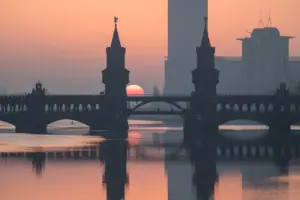 Silhouet van de Oberbaumbrücke in Berlijn bij zonsopgang, met de torens en de roodachtige zon weerspiegeld in het kalme water van de Spree.