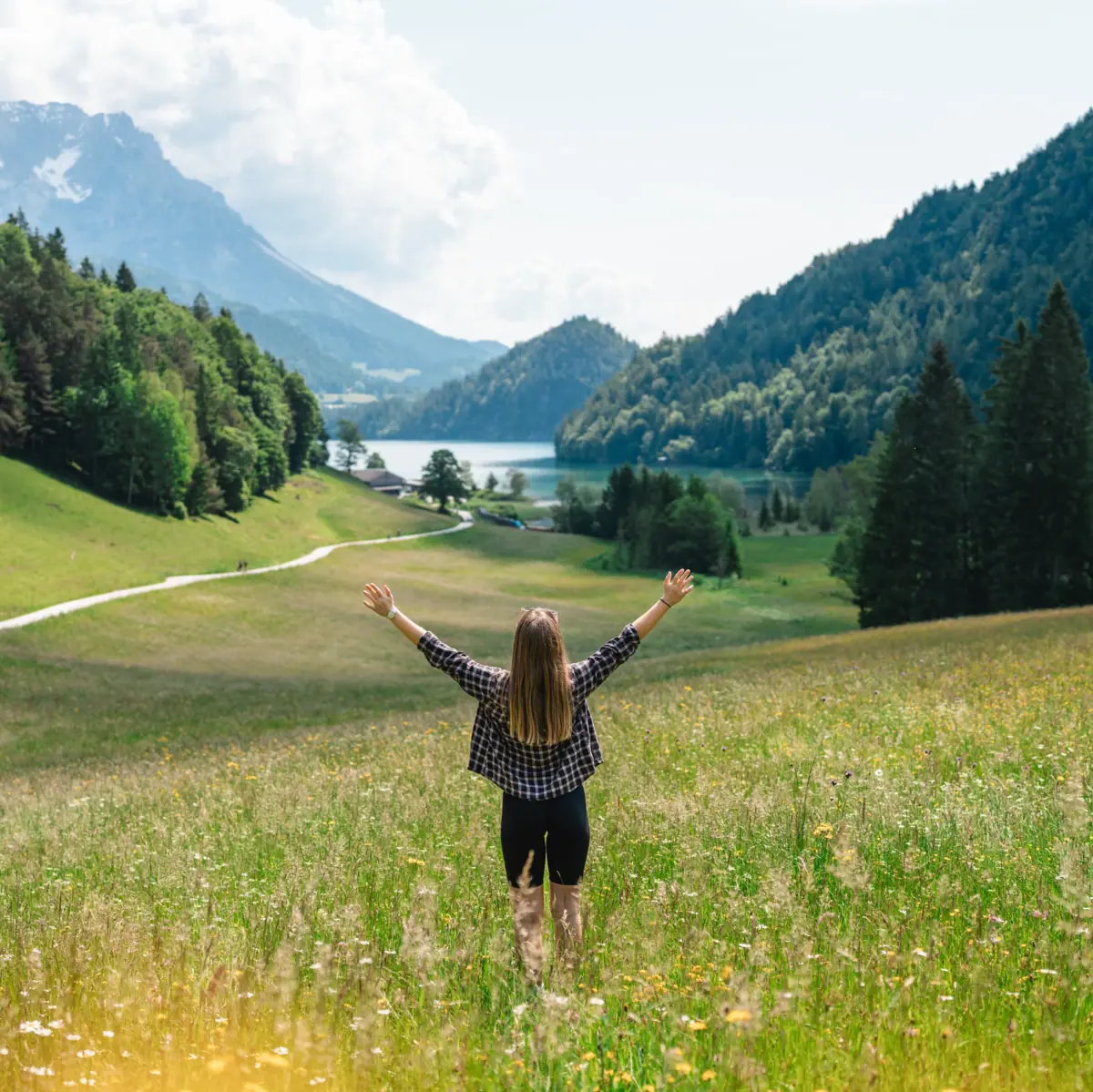 Kitzbüheler Alpen Een vrouw staat in een veld en strekt haar armen omhoog. Op de achtergrond zijn bergen te zien.