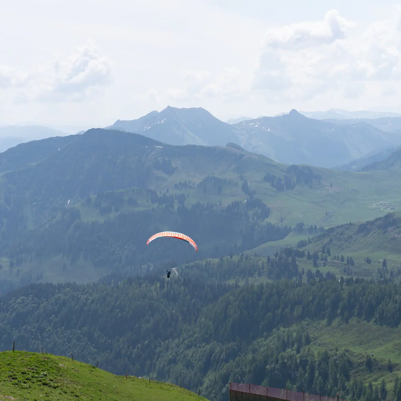 Een persoon aan het paragliden boven een vallei met bergen en wolken op de achtergrond.