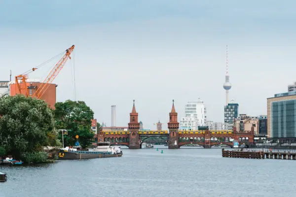 Gezicht op de bakstenen gotische Oberbaumbrücke in Berlijn met een gele metro en de televisietoren van Berlijn op de achtergrond onder een bewolkte hemel