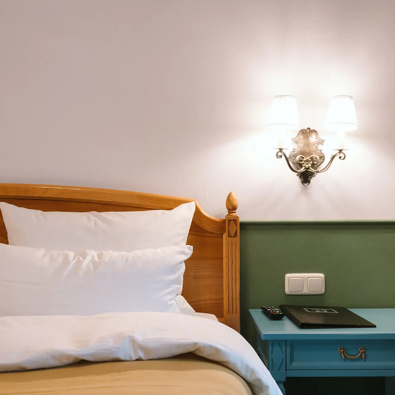 Een bed met een houten hoofdeinde voor een groen-witte muur in een stijlvol ingerichte hotelkamer in het HENRI Hotel Garmisch-Partenkirchen.