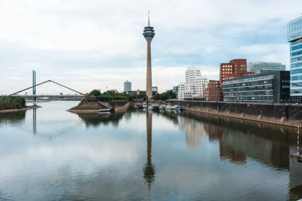 De skyline van Düsseldorf met een rivier op de voorgrond en een toren op de achtergrond.