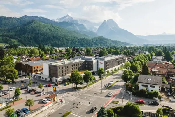 aja Garmisch-Partenkirchen De aja Garmisch-Partenkirchen met veel gebouwen en bomen onder een bewolkte hemel en bergen op de achtergrond.