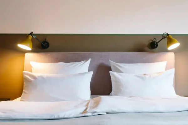 Hotelkamer HENRI Hotel Garmisch-Partenkirchen Een bed met witte kussens en een lamp in een hotelkamer in het HENRI Hotel in Garmisch-Partenkirchen.