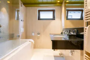 Badkamer in de suite van HENRI in Garmisch-Partenkirchen Badkamer met wastafel en badkuip, voorzien van kranen en een spiegel.
