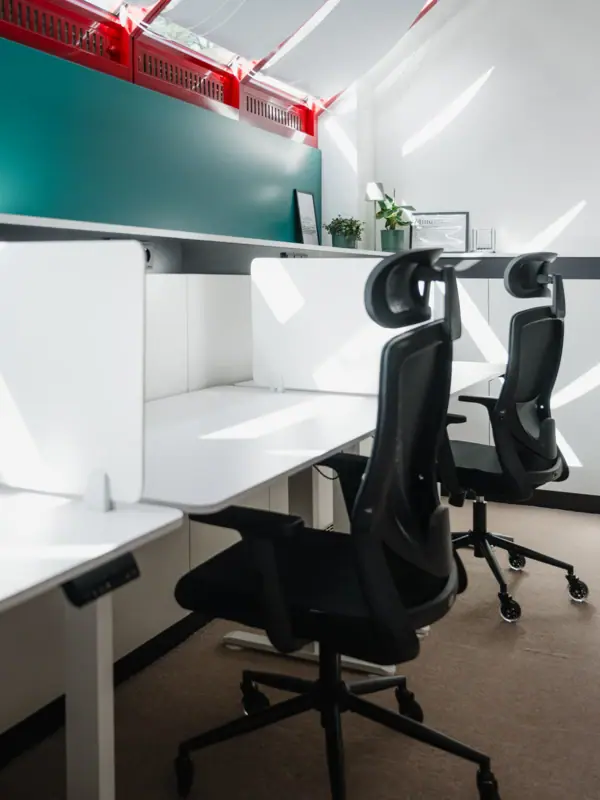 Een ruimte met witte bureaus en stoelen.