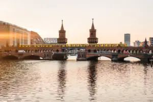 Zicht op de bakstenen gotische Oberbaumbrücke in Berlijn bij zonsondergang met een gele metro en weerspiegeling in het water.