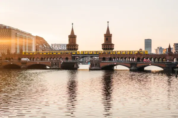 Zicht op de bakstenen gotische Oberbaumbrücke in Berlijn bij zonsondergang met een gele metro en weerspiegeling in het water.