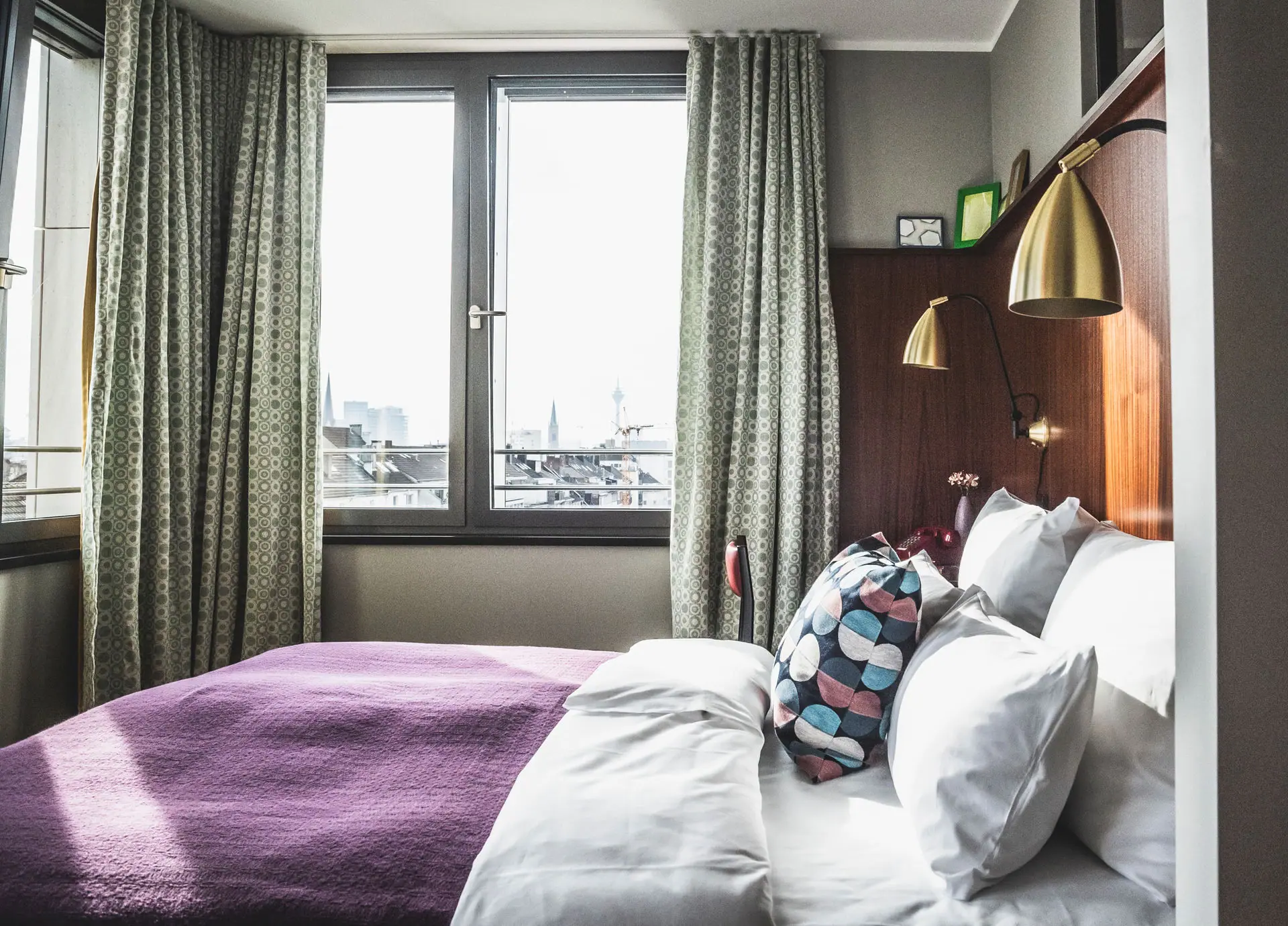 HENRI Düsseldorf Een bed met kussens en een lamp in een kamer met ramen.