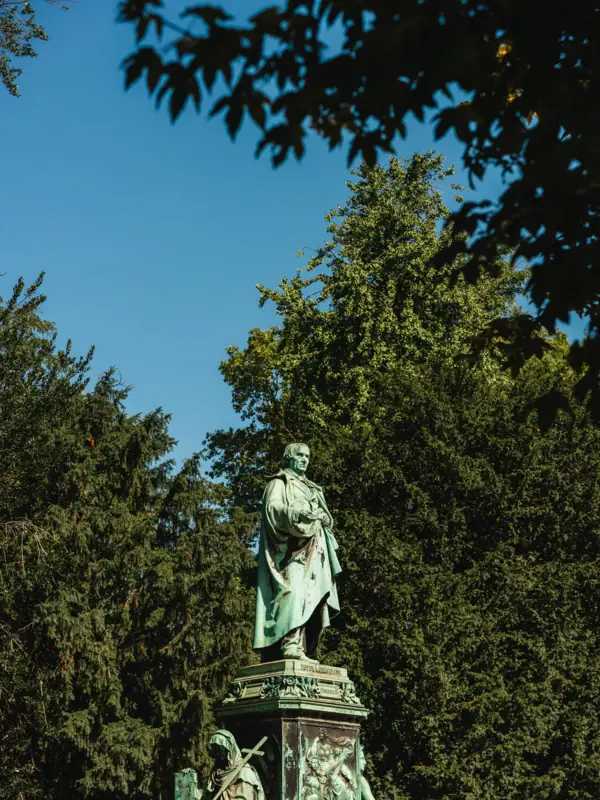 Standbeeld van Peter von Cornelius in Düsseldorf Standbeeld van een man in een gewaad, in de open lucht tegen een blauwe hemel.