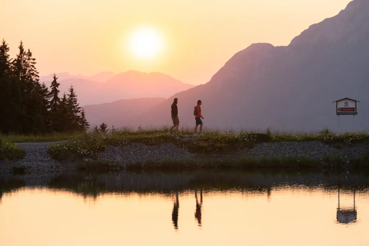 Zonsondergang voor een bergmeer Twee mensen lopen op een heuvel bij een meer.