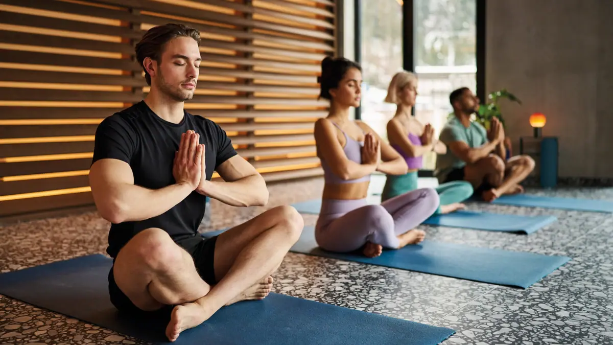 Een groep mensen zit op yogamatten met de handen gevouwen.