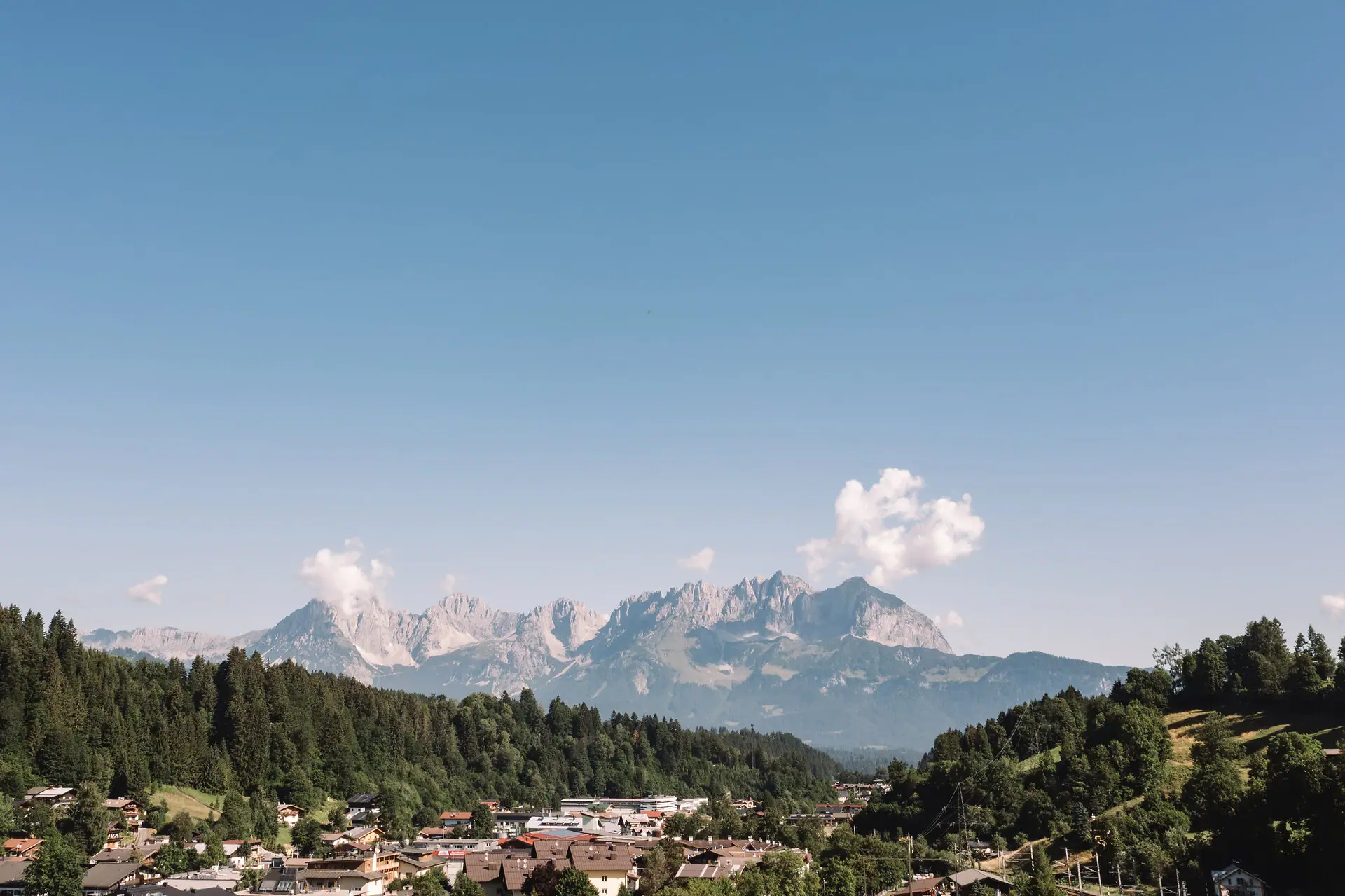 Kitzbüheler Alpen Een stad in de bergen met bomen en een heldere hemel.