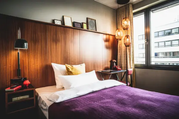 Bed met een paarse deken en kussens in een kamer met een raam.
