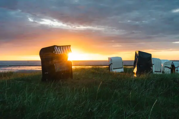 Strandstoelen in Cuxhaven op een met gras begroeid terrein, met de zonsondergang op de achtergrond.