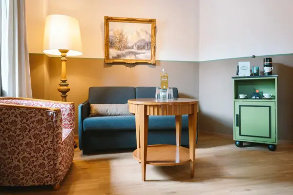 Een zithoek met bank, fauteuil en tafel in een hotelkamer in het HENRI Hotel in Garmisch-Partenkirchen.