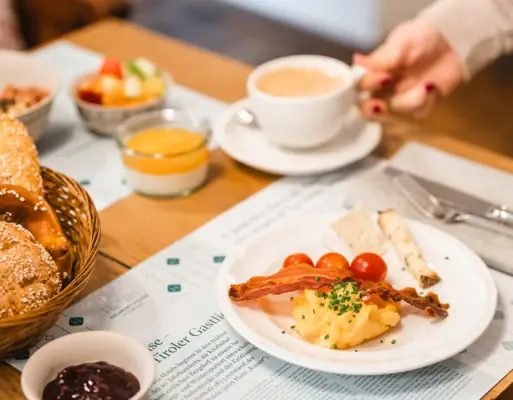 Eén persoon houdt een kop koffie en een bord eten vast.