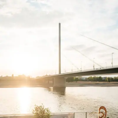 HENRI Brug Düsseldorf Een groep mensen zit op stoelen aan de oever van de rivier.