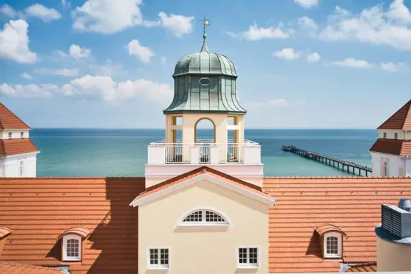 Kurhaus Binz Een gebouw met een toren op de voorgrond en een pier op de achtergrond.