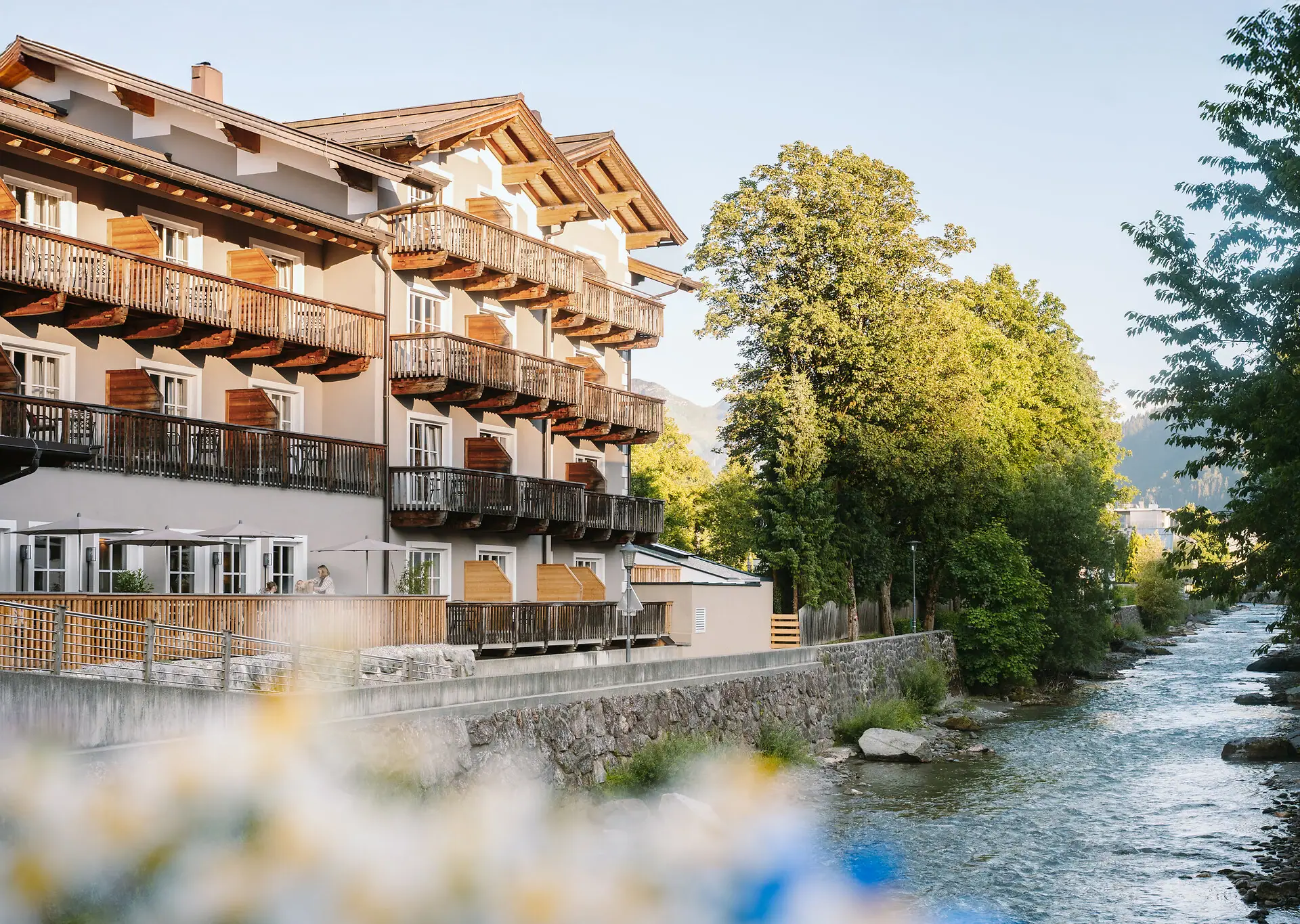 HENRI Kitzbühel buitenaanzicht Een gebouw met balkons en een rivier op de voorgrond.