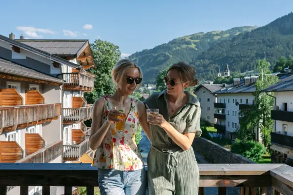 Twee vrouwen staan op een balkon met uitzicht op bergen en bomen.