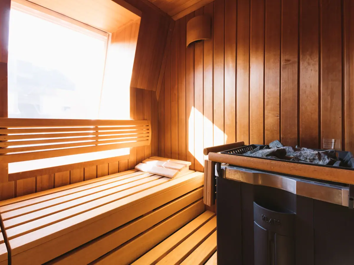 Houten sauna met kachel en raam in het interieur.