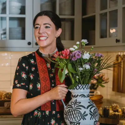 Vrouw houdt een vaas met bloemen vast en glimlacht.