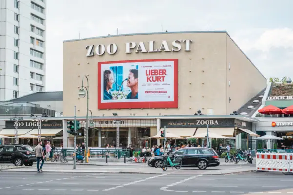De opvallende gevel van de historische bioscoop Zoo Palast in Berlijn overdag met de huidige filmreclame en het stadsverkeer op de voorgrond