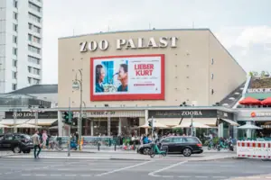 De opvallende gevel van de historische bioscoop Zoo Palast in Berlijn overdag met de huidige filmreclame en het stadsverkeer op de voorgrond