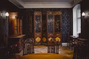 HENRI Hotel Berlijn: interieur van de salon met kamerscherm Een prachtig ingerichte salon in HENRI Berlin met donker patroonbehang, een antiek meerdelig kamerscherm met goudschilderingen en statige houten meubels.