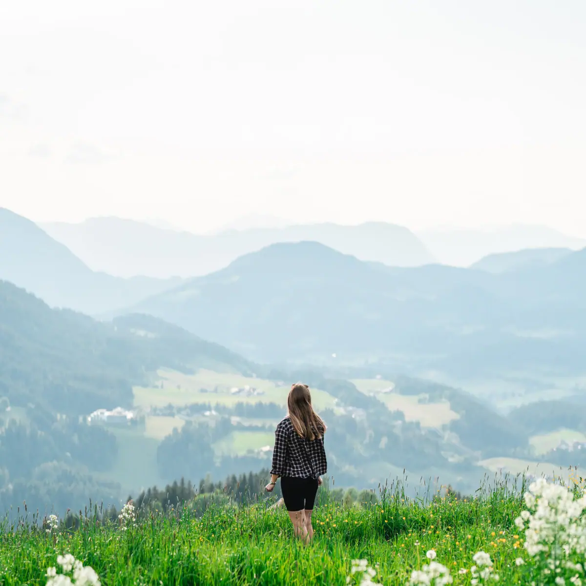 Vrouw in de bergen Een vrouw staat op een met gras begroeide heuvel met bergen op de achtergrond.