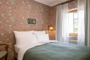 HENRI GAP Petit Kabinett Bed met een groene sprei en een lamp tegen een achtergrond van bloemenbehang.
