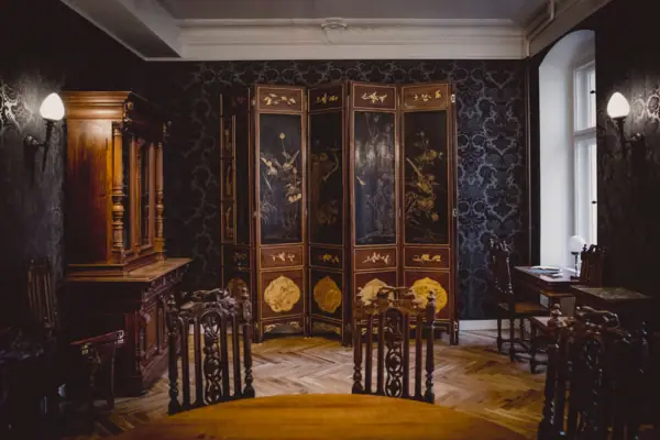 Een prachtig ingerichte salon in HENRI Berlin met donker patroonbehang, een antiek meerdelig kamerscherm met goudschilderingen en statige houten meubels.