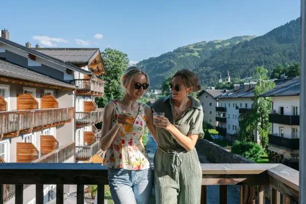 Twee vrouwen staan op een balkon met uitzicht op bergen en bomen.