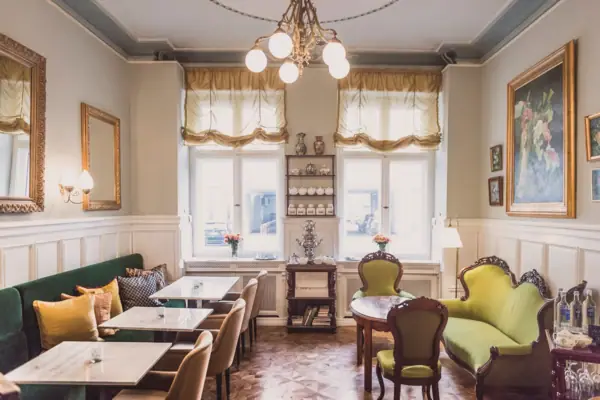 Een lichte, klassiek ingerichte salon in HENRI Berlin met groene fluwelen banken, marmeren tafels, een antieke samovar en statige olieverfschilderijen aan de muren.