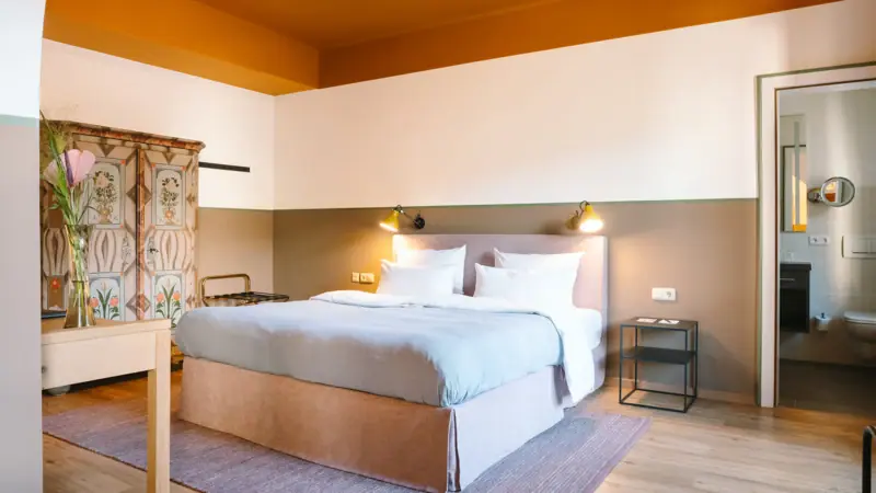 Een hotelkamer in het HENRI Hotel Garmisch-Partenkirchen met een knus bed en een oude kledingkast.