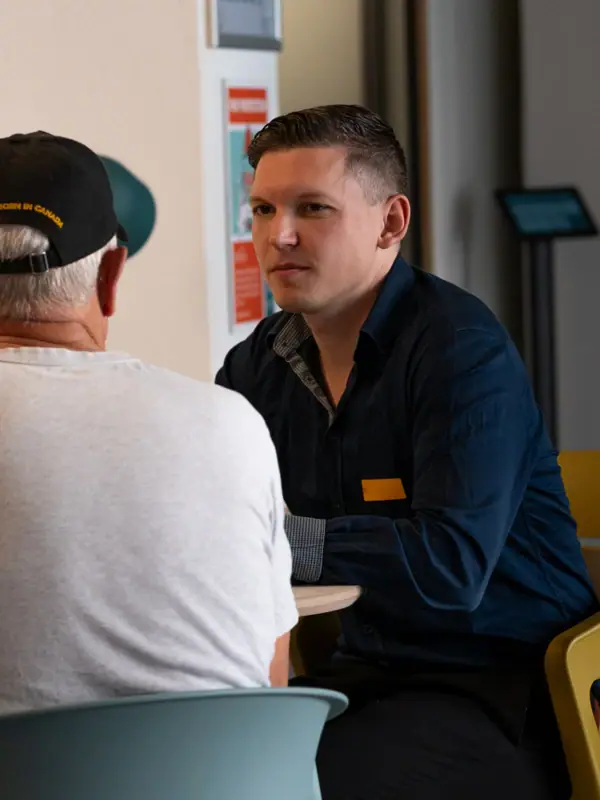 Een man zit aan een tafel met een andere man in een wit overhemd.