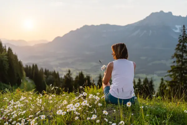 Uitzicht op het Alpenpanorama Een vrouw zit op een heuvel met bloemen.