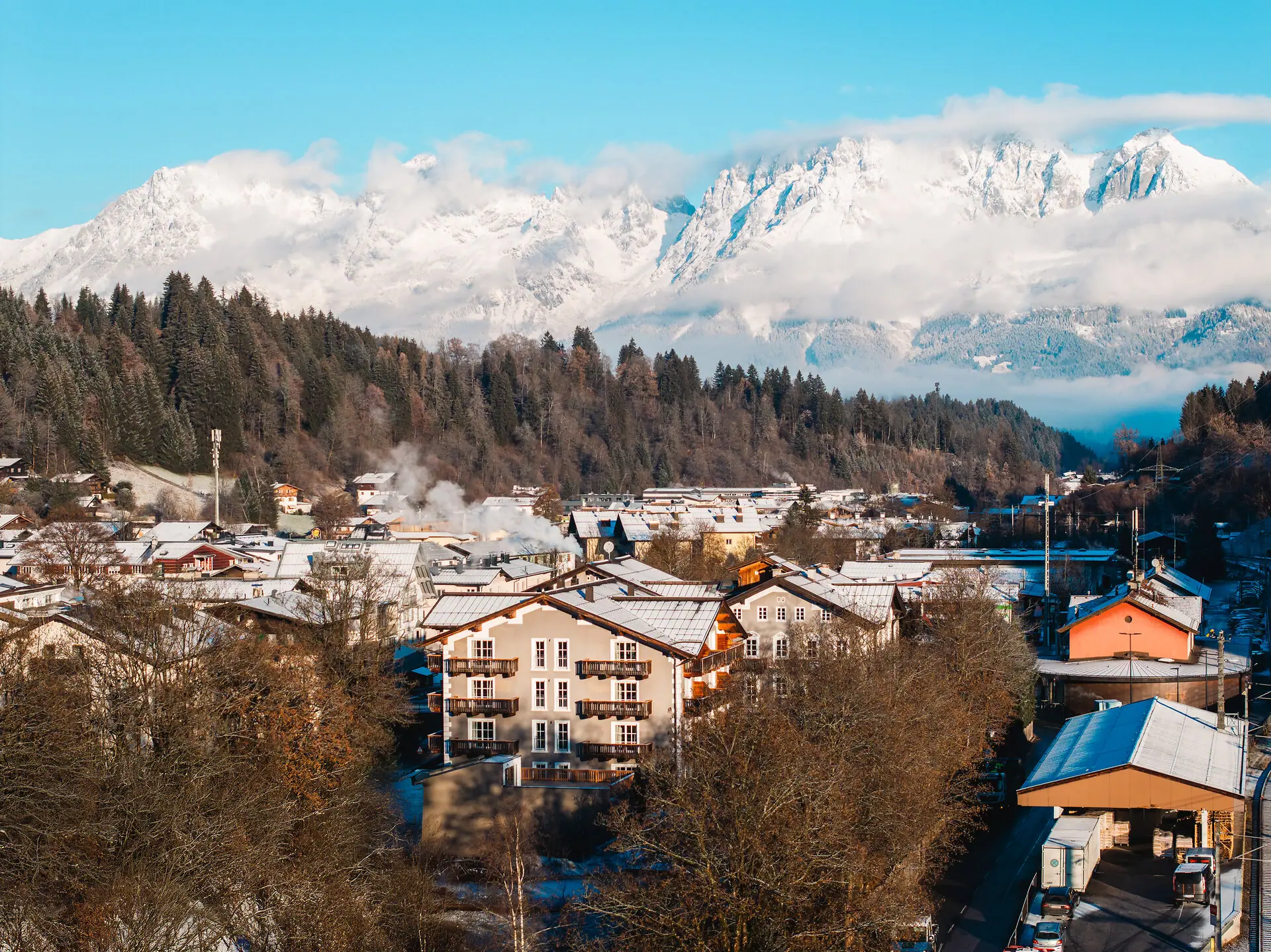 HENRI Kitzbühel drone uitzicht Een bergdorpje met besneeuwde bergen op de achtergrond.
